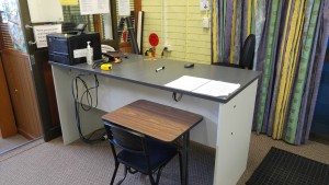 The high teacher's desk creates a physical barrier from students. It is in the back-right corner of the room, next to the entrance.
